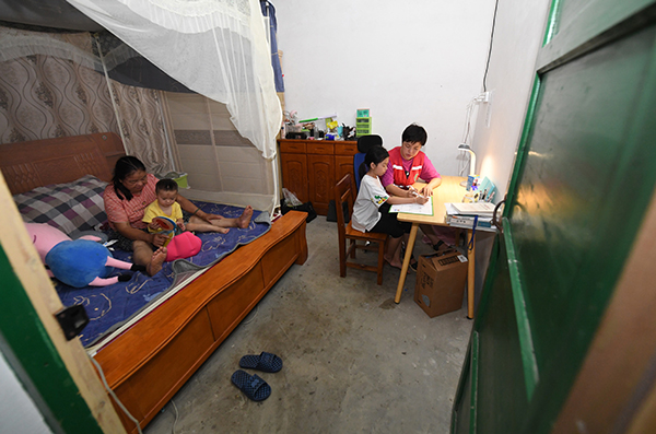 毛鑫）在村里的临时住房里，毛鑫（右一）指导女儿做作业，她的母亲和小外孙在床上玩耍。 新华社发 2.jpg