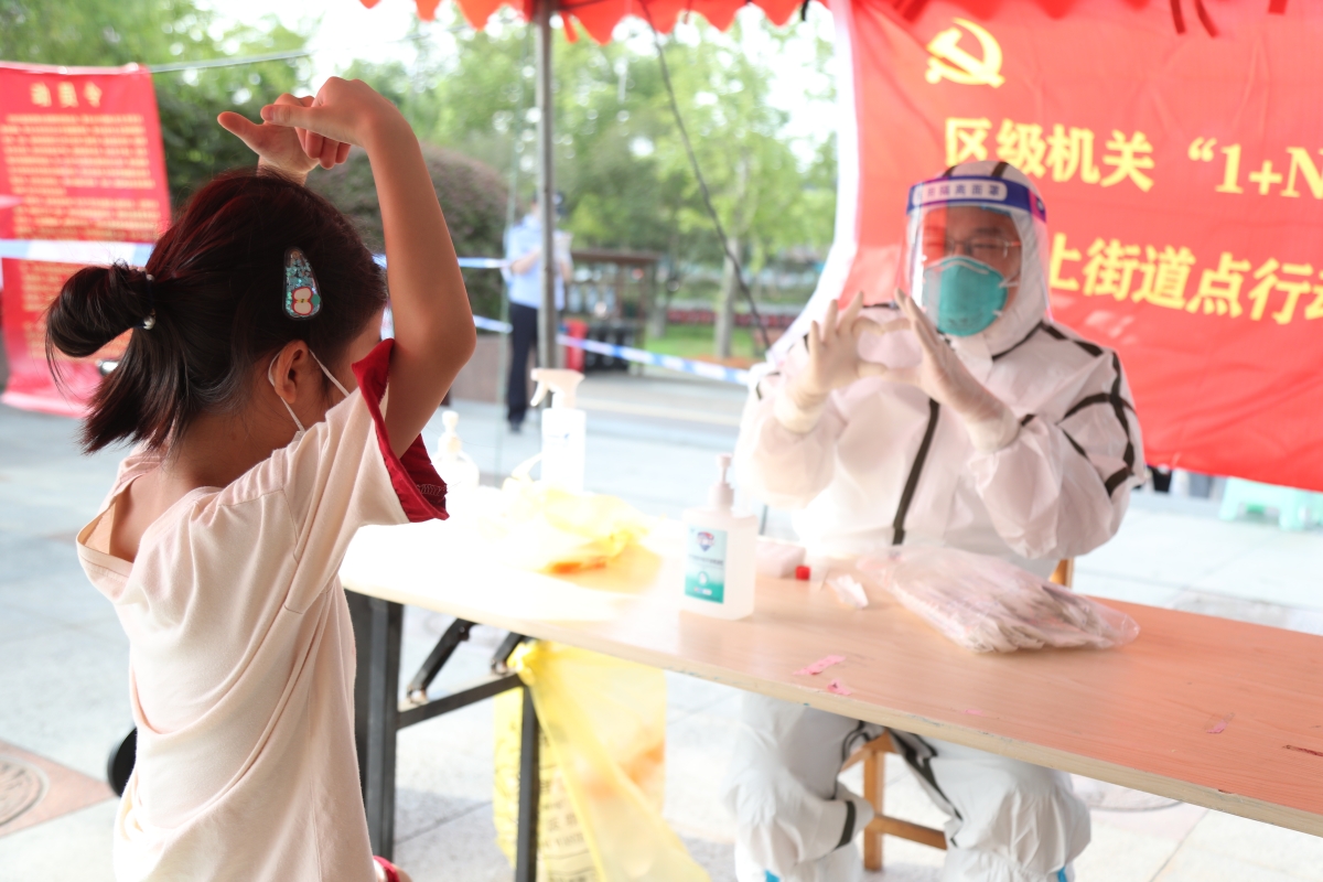 图2扬州市邗江区邗上街道来鹤台广场核酸检测点，小女孩和志愿者互相比心。.jpg